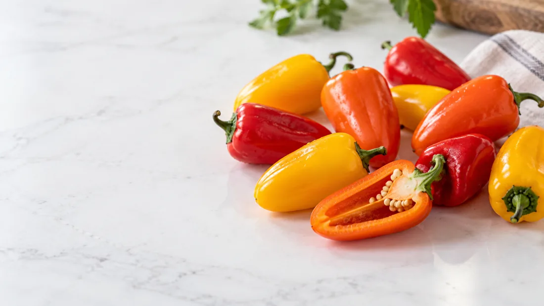Fresh mini sweet peppers showing whole fruit and a small cavity Fresh finger-sized mini sweet peppers, whole and halved